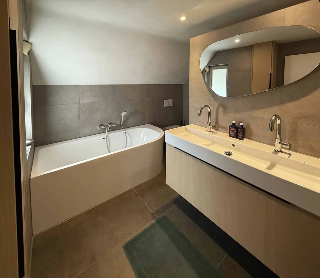 Badkamer met ligbad, dubbele wastafel en betonlook tegels