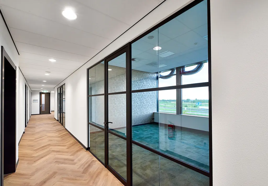 Gang met glaswand in donkere aluminium profielen en een wit plafond