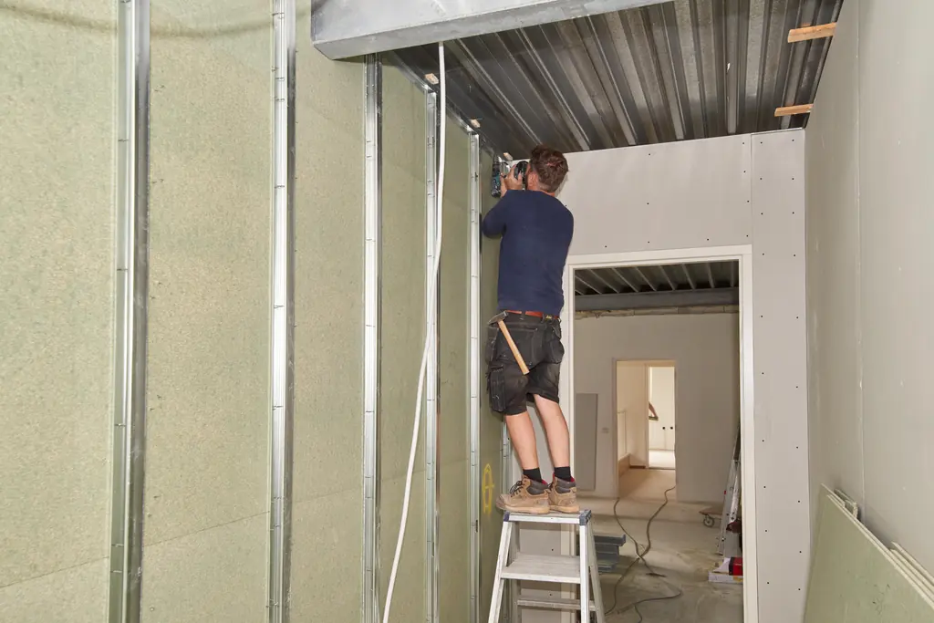 Monteur op een trap werkt aan een metal stud wand met isolatie
